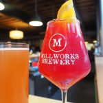 orange kombucha in beer glass next to pink mocktail in wine glass